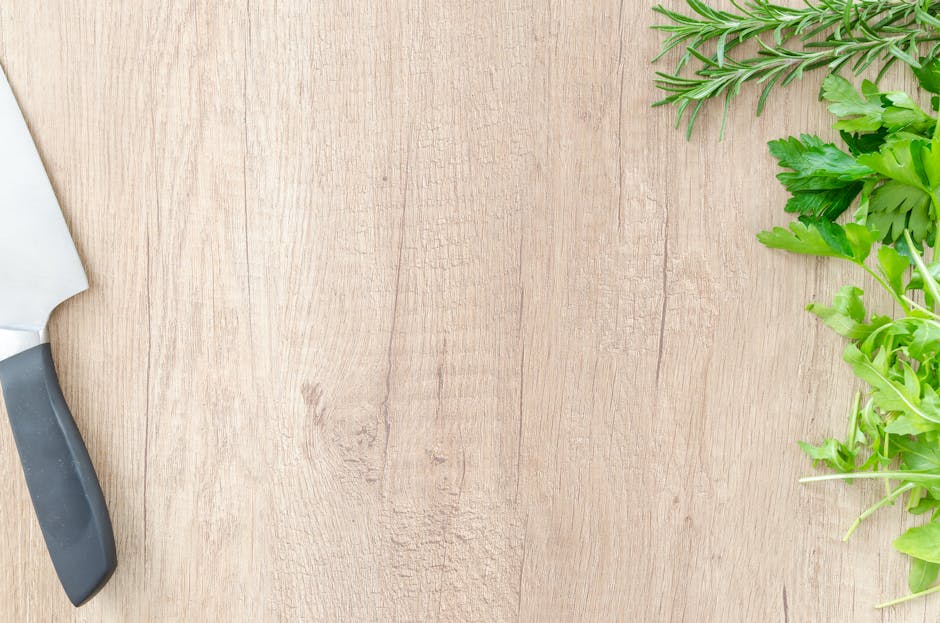 Top view of fresh rosemary and parsley with a chef's knife on a wooden surface, offering ample copyspace.