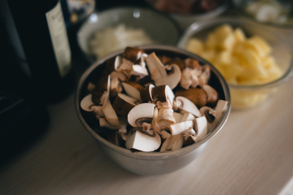 Close-up of fresh sliced mushrooms in a metal bowl on a kitchen counter.