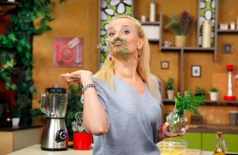 Cheerful woman in a modern kitchen, playfully holding fresh dill, surrounded by kitchen appliances.